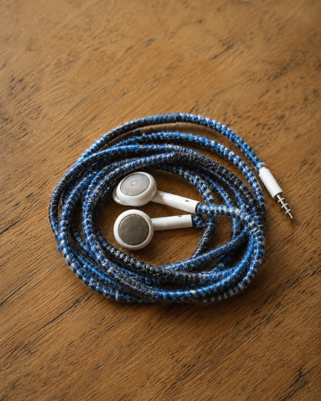 Auriculares blancos con el cable envuelto en tejido azul, rojo y negro